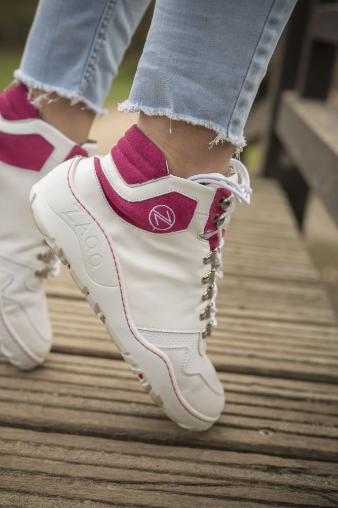 Una persona que lleva las botas VAQATION Pink Waterproof ZAQQ, combinadas con jeans azul claro con dobladillos deshilachados, está de pie con confianza sobre una superficie de madera.