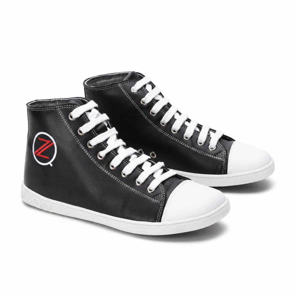 Un par de zapatillas altas negras clásicas de ZAQQ CHUQQS tiene cordones blancos y punteras que muestran un llamativo logo Z en rojo y blanco. Las suelas están hechas de goma de caucho resistente, lo que le da a los zapatos un aspecto moderno y ligeramente desgastado.