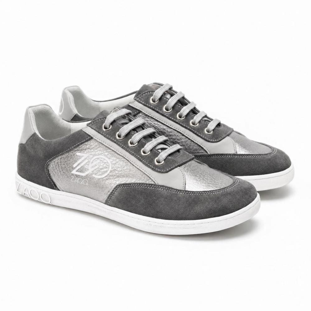 Un par de zapatillas OQTAV Grey de ZAQQ, fabricadas con gamuza aterciopelada e inserciones texturizadas. Con cordones plateados y el inconfundible logo de Zagoo en el lateral y el talón, estos elegantes zapatos se presentan uno al lado del otro sobre un fondo blanco.