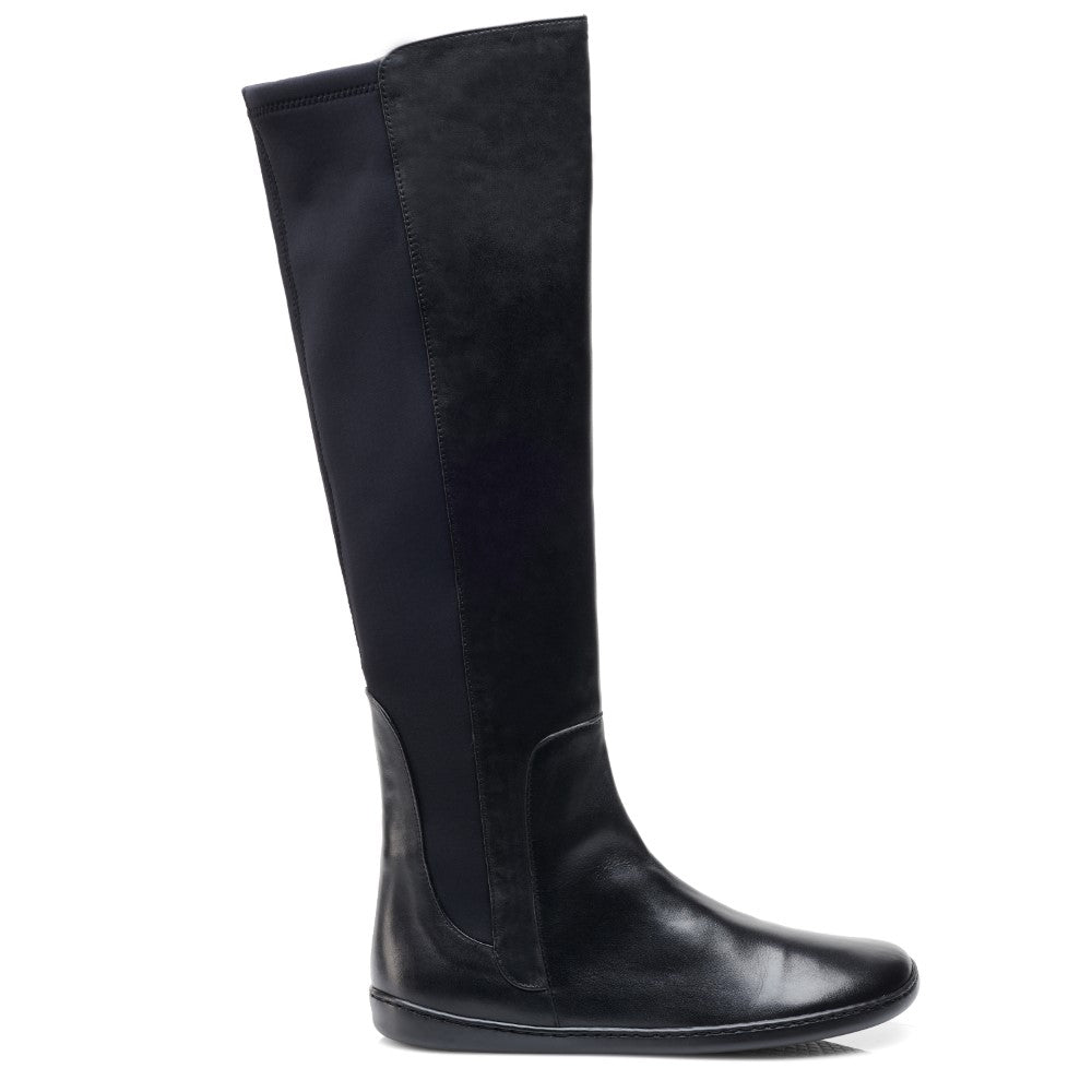 Der QATCH Winter Black Boot von ZAQQ wird vor einem weißen Hintergrund präsentiert. Dieser hohe schwarze Lederstiefel hat eine glatte, glatte Oberfläche mit einer flachen Kautschuksohle und reicht bis knapp unters Knie. Die dem Betrachter zugewandte Seite hebt detaillierte Nähte und subtile Strukturkontraste hervor.